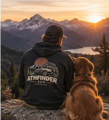 Man in an ATHFINDER hoodie and his dog watching the sunset over a lake